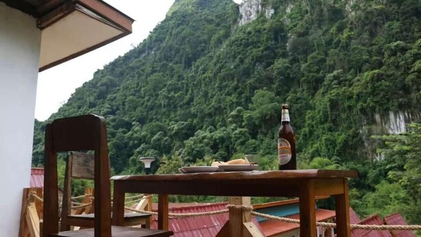 Ein Tisch mit einer Bierflasche, Tellern und einem Stuhl in einem Zimmer mit Blick auf einen bewaldeten Berg.
