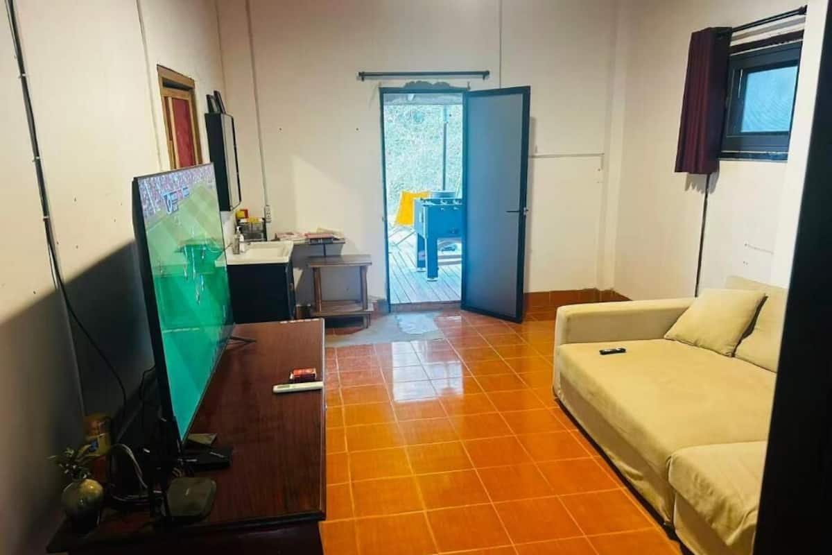 A room with a wooden desk, a white sofa, a television, and a door leading to an outdoor area with a table and chairs.