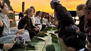 Eine Gruppe Menschen sitzt bei Sonnenuntergang auf Matten im Freien und isst Blättergerichte.