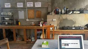 Eine rustikale Küche mit einem Laptop auf einem Tisch, Holzstühlen und einem Regal mit diversen Küchenutensilien.