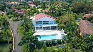 A modern two-story house with a swimming pool, surrounded by lush greenery and palm trees. - 5BR Hispaniola Villa in Sosua (Sosúa)