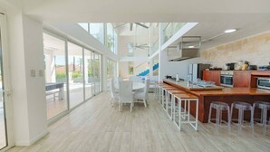 A modern kitchen with a central island, bar stools, and a view through large windows. - 5BR Hispaniola Villa in Sosua (Sosúa)
