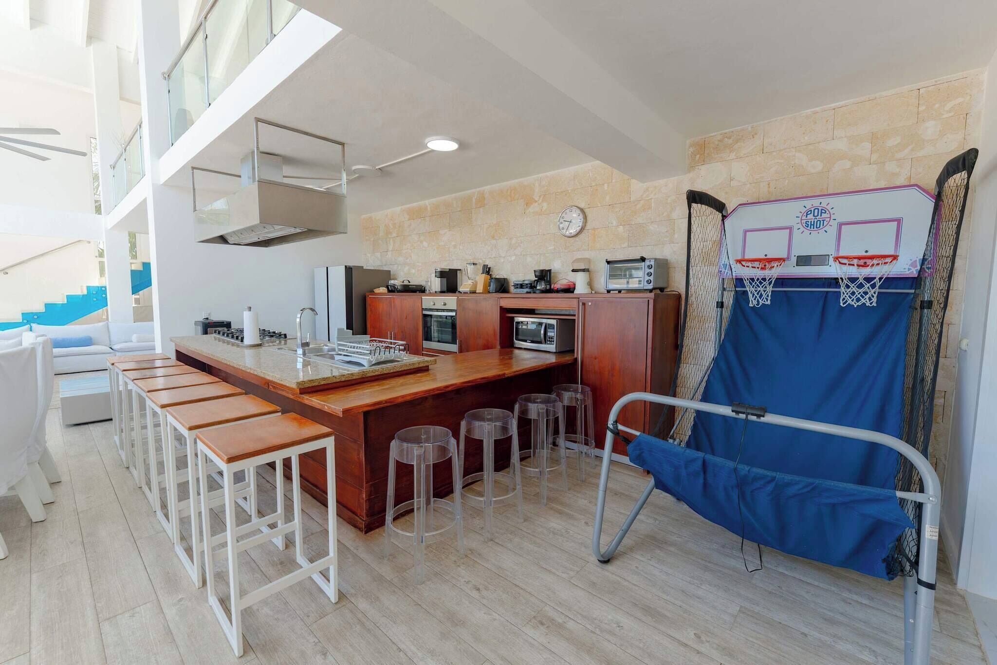 A modern kitchen with a bar area, wooden stools, and a basketball hoop.