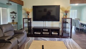 A living room with a sofa, a coffee table, a TV, and a dining area. - Spacious 4-bedroom 2 bath house equipped with AC. Sleeps up to 12 people. (Lawton)