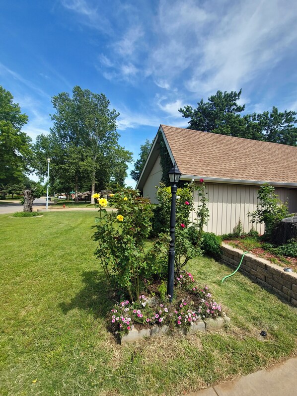 A residential building with a sloped roof, a garden with flowers, and a clear blue sky.