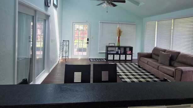 A living room with a checkered rug, a sofa, a ceiling fan, and a dining area with a table and chairs. - Spacious 4-bedroom 2 bath house equipped with AC. Sleeps up to 12 people. (Lawton)