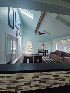 A living room with a checkered rug, a sofa, a ceiling fan, and a dining area with a table and chairs.