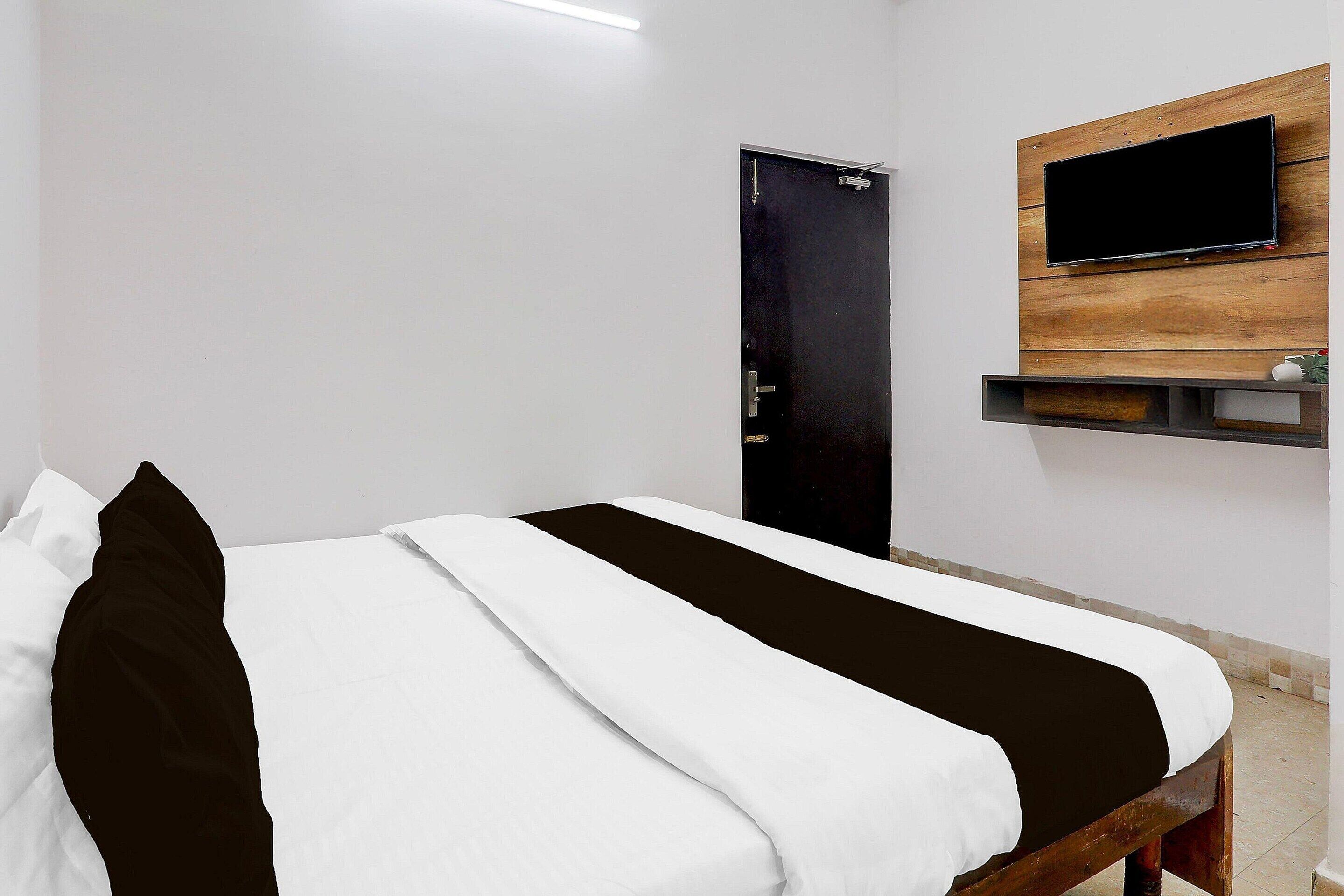 Ein Zimmer mit einem Bett, einer Tür, einem Wandfernseher und einem Regal.