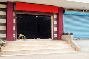 Une entrée d’immeuble avec une porte noire, des auvents rouges et bleus, et des marches menant à l’entrée.