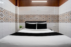 Une chambre d’hôtel avec un lit, une table de chevet, une plante et des carreaux muraux à motifs.