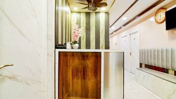 A hotel reception area with a marble wall, a wooden panel, a ceiling fan, a clock, and a reception desk.