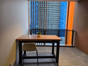 Un petit balcon avec une table et une chaise, un pot de fleurs et une vue sur un immeuble en échafaudage.