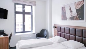 Een hotelkamer met een bed, een bureau, een stoel, een raam en een foto aan de muur.