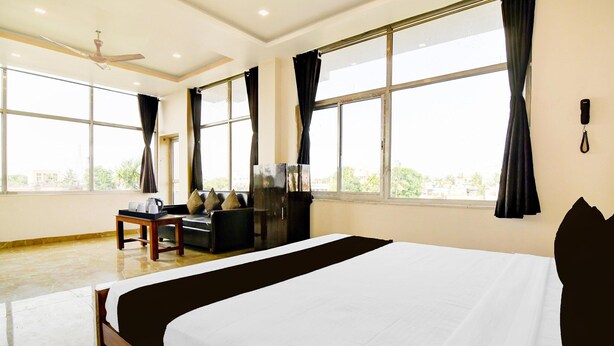 A hotel room with a large bed, a desk with a chair, a television, and a window with curtains. - Deluxe Howrah Tanima Villa (Howrah)