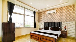 A bedroom with a large bed, a wooden nightstand, a wall-mounted air conditioner, and a window with curtains. - Deluxe Howrah Tanima Villa (Howrah)
