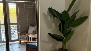 A room with a sliding door leading to a balcony, a potted plant, a small table with a lamp, and a chair with a cushion. - Ingonyama Rest (Marloth Park)