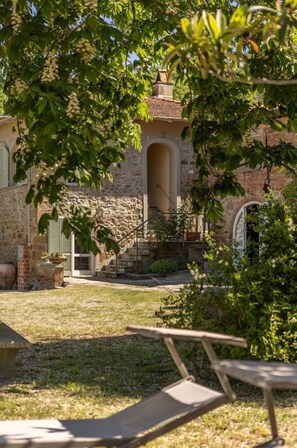 Un edificio in pietra con un giardino, una panchina e una scalinata che conduce a una porta.