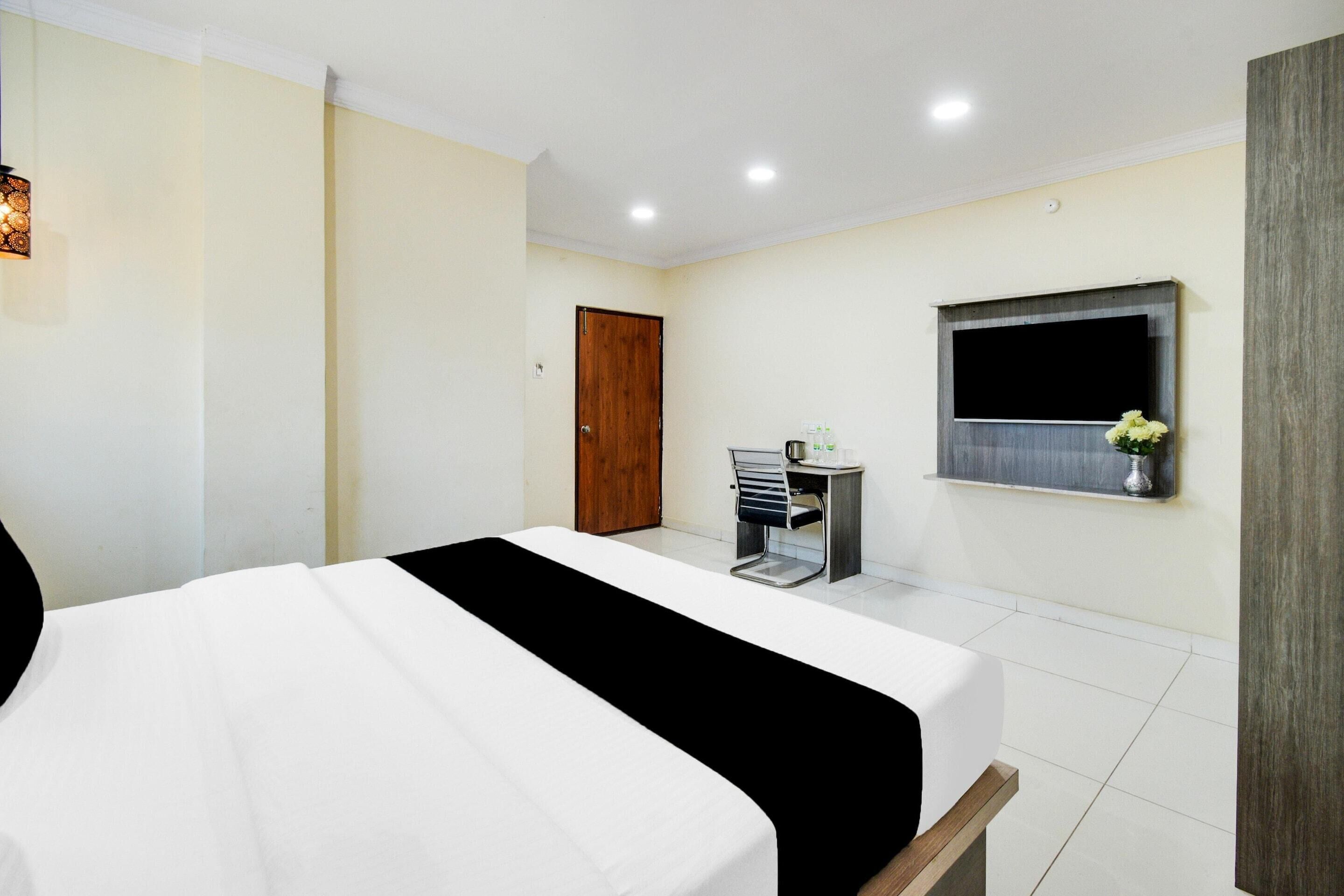A hotel room with a bed, a small desk with a chair, a TV mounted on the wall, and a door.