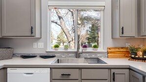A kitchen with a double sink, cabinets, a dishwasher, and potted plants on the windowsill. - Elegant Fairway Frontage Retreat-Eagle Crest Resort 3BD 2.5BA Centrally Located (Redmond)
