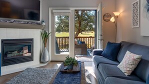 A living room with a fireplace, a sofa, a TV, and a view of a deck. - Elegant Fairway Frontage Retreat-Eagle Crest Resort 3BD 2.5BA Centrally Located (Redmond)