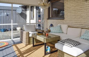 A sunlit patio with wicker furniture, a glass table, and a white sofa with patterned cushions. - Lovely home in Simrishamn with WiFi (Simrishamn)