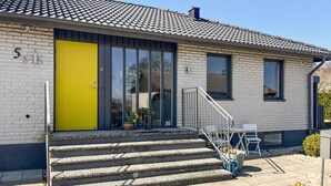 Rakennuksessa on keltainen ovi, portaikko ja pieni ulkona oleva oleskelualue.