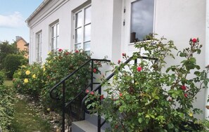 Ein weißes Gebäude mit einer schwarzen Treppe, die zu einer Tür führt, umgeben von Grünpflanzen und Blumen.