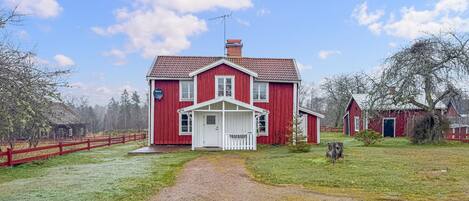 A red farmhouse with a white porch, a gravel driveway, and a fenced yard.