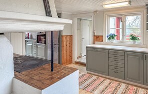 Una cocina con una isla central, armarios de madera, un ventanal con plantas y una puerta que conduce a otra habitación.