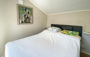 Un dormitorio con cama, cabecera, mesita de noche, lámpara de pared y un cuadro abstracto enmarcado.