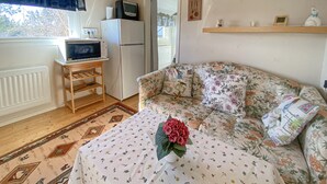 Una habitación acogedora con sofá, un pequeño televisor sobre un mueble, un refrigerador y una ventana con cortinas.