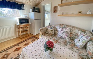 Una habitación acogedora con sofá, un pequeño televisor sobre un mueble, un refrigerador y una ventana con cortinas.