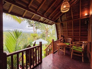 A wooden deck with a railing, a table, and two chairs, overlooking a lush landscape. - Casa Vella Cottages by AGATA (Petang)