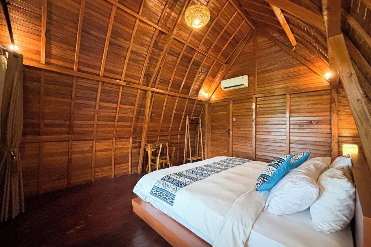 Una habitación de madera con una cama, una escalera y un equipo de aire acondicionado.