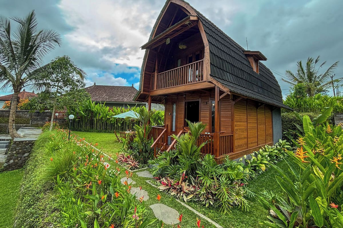 Una casa de madera con balcón, rodeada de abundante vegetación y un jardín.