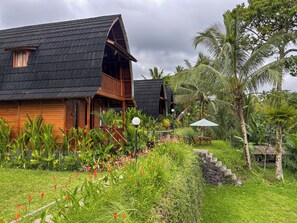 A wooden house with a sloped roof, surrounded by lush greenery and palm trees. - Casa Vella Cottages by AGATA (Petang)