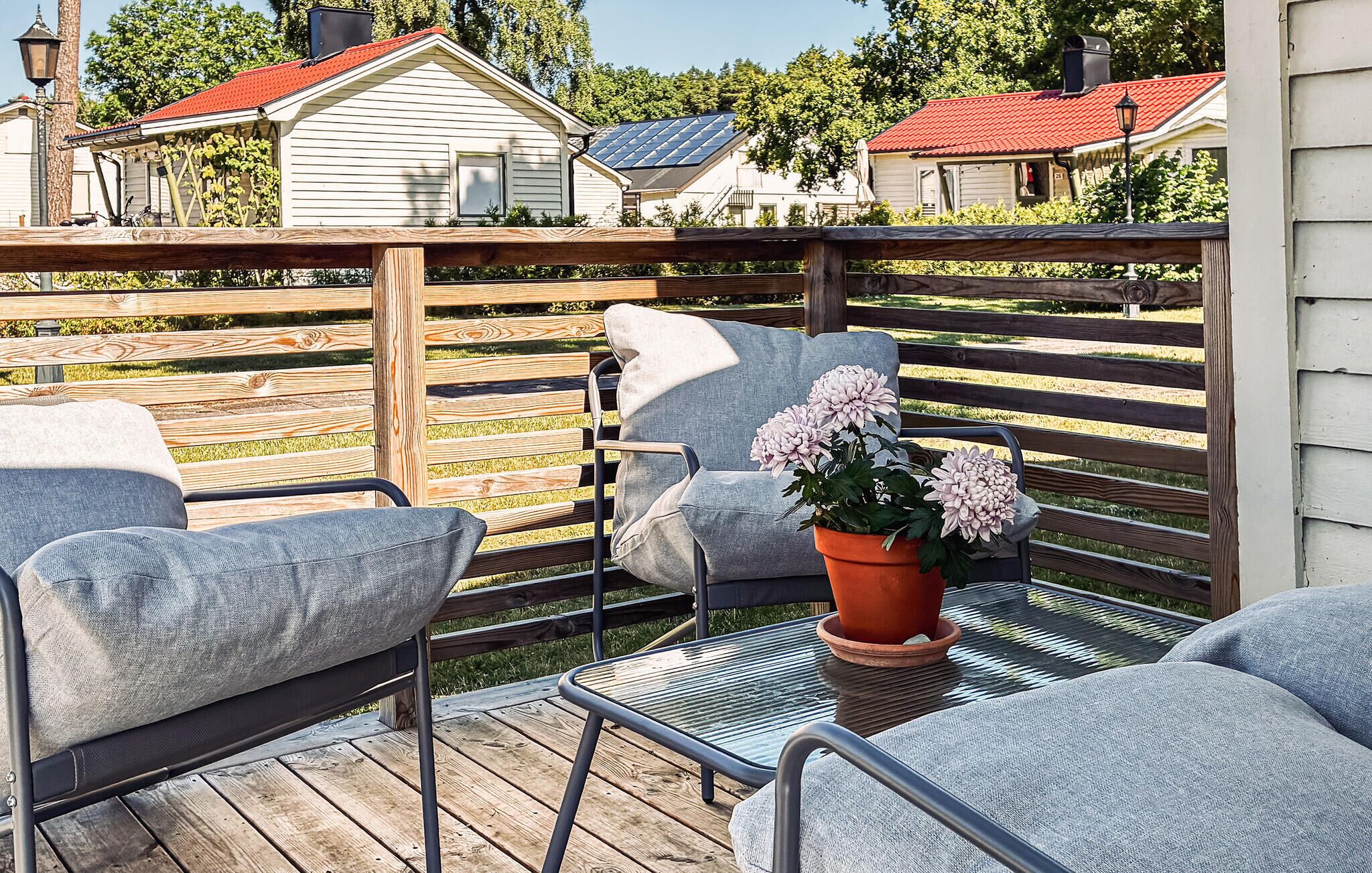 Una terraza de madera con mobiliario exterior, incluyendo dos sillas y una mesa, y una maceta con flores.