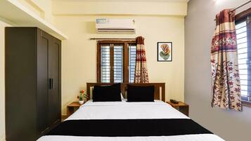 A bedroom with a bed, an air conditioner, a window with curtains, a wardrobe, and a bedside table with a phone.