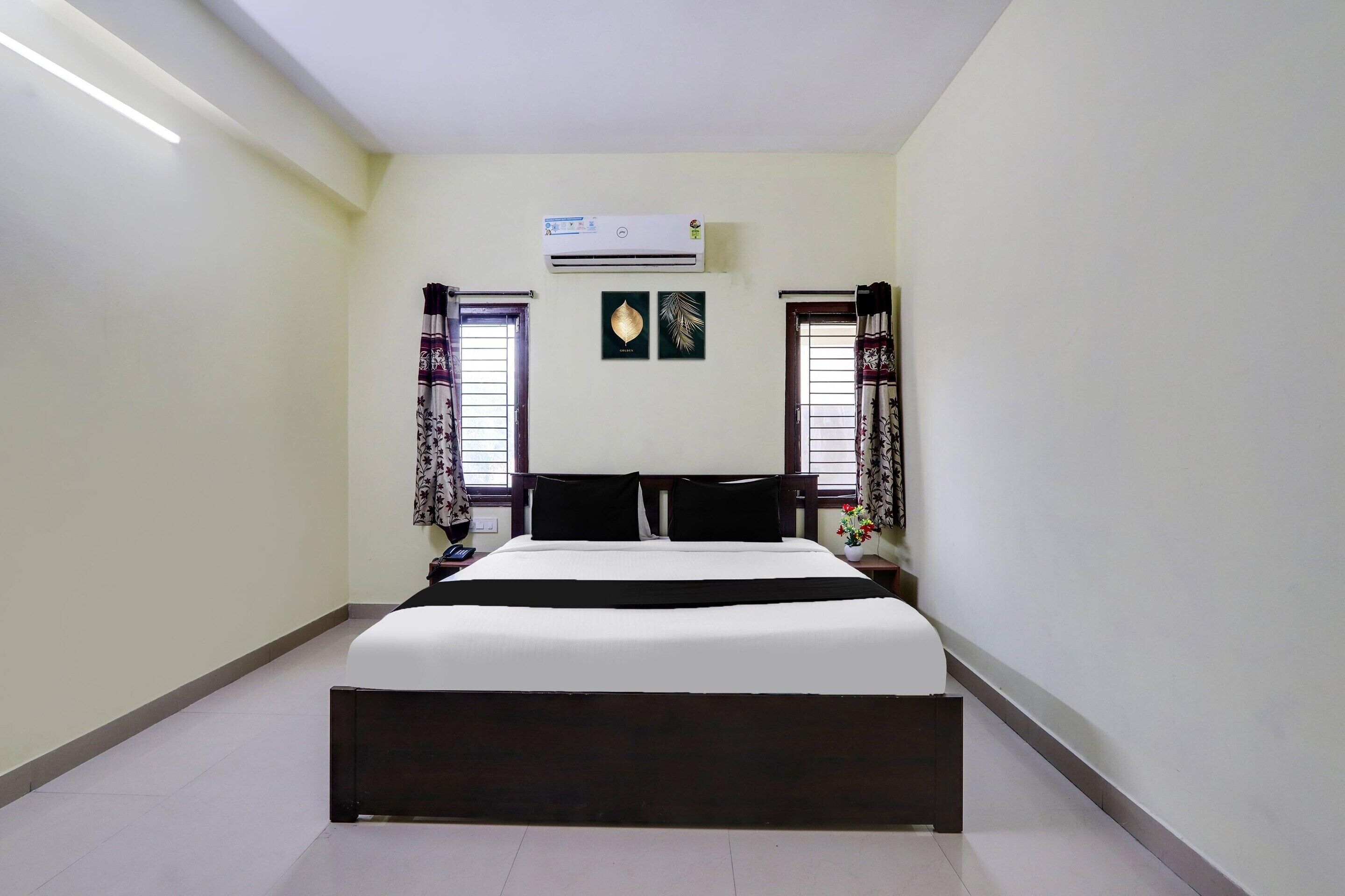 Habitación de hotel con cama, aire acondicionado, dos ventanas con cortinas y un aire acondicionado de pared.