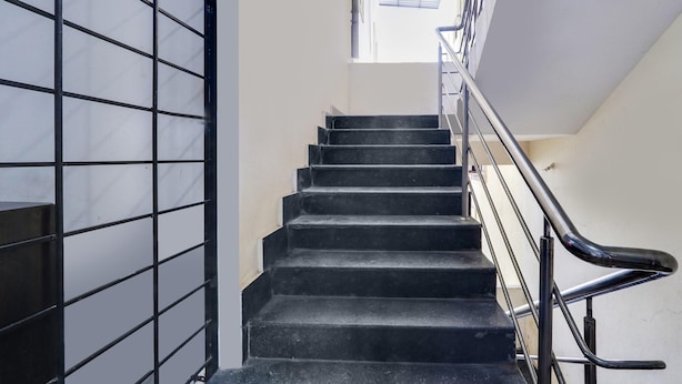 A staircase with a metal railing, a grid-like wall on the left, and a window at the top. - Deluxealpine Glow Pinnacle (Hyderabad)