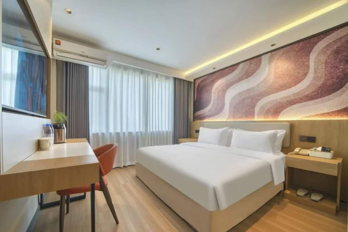Una habitación de hotel moderna con una cama grande, un escritorio, una silla, una mesita de noche y una pared con un diseño ondulado.