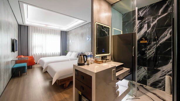 Habitación de hotel con cama, escritorio con espejo, ducha con azulejos de mármol y televisión en la pared.