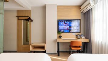 A hotel room with a wooden desk, a television, a chair, and a bed.