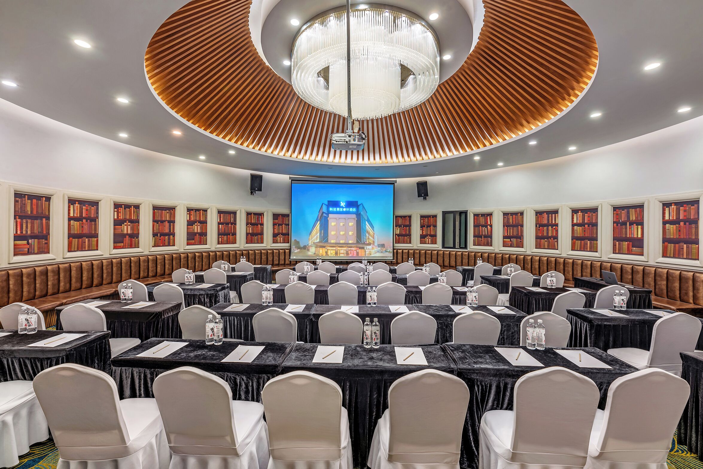 A conference room with round tables, chairs, a large screen, and bookshelves.