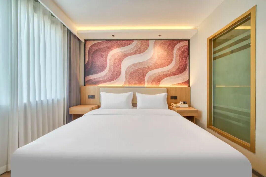 Une chambre d’hôtel avec un grand lit, une table de chevet avec un téléphone et une œuvre d’art accrochée au mur.