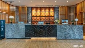 Un mostrador de recepción con frente de mármol, paneles de madera en las paredes y un monitor que muestra la imagen de un edificio.
