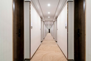 Un pasillo de hotel con alfombra estampada, puertas de madera e iluminación empotrada.