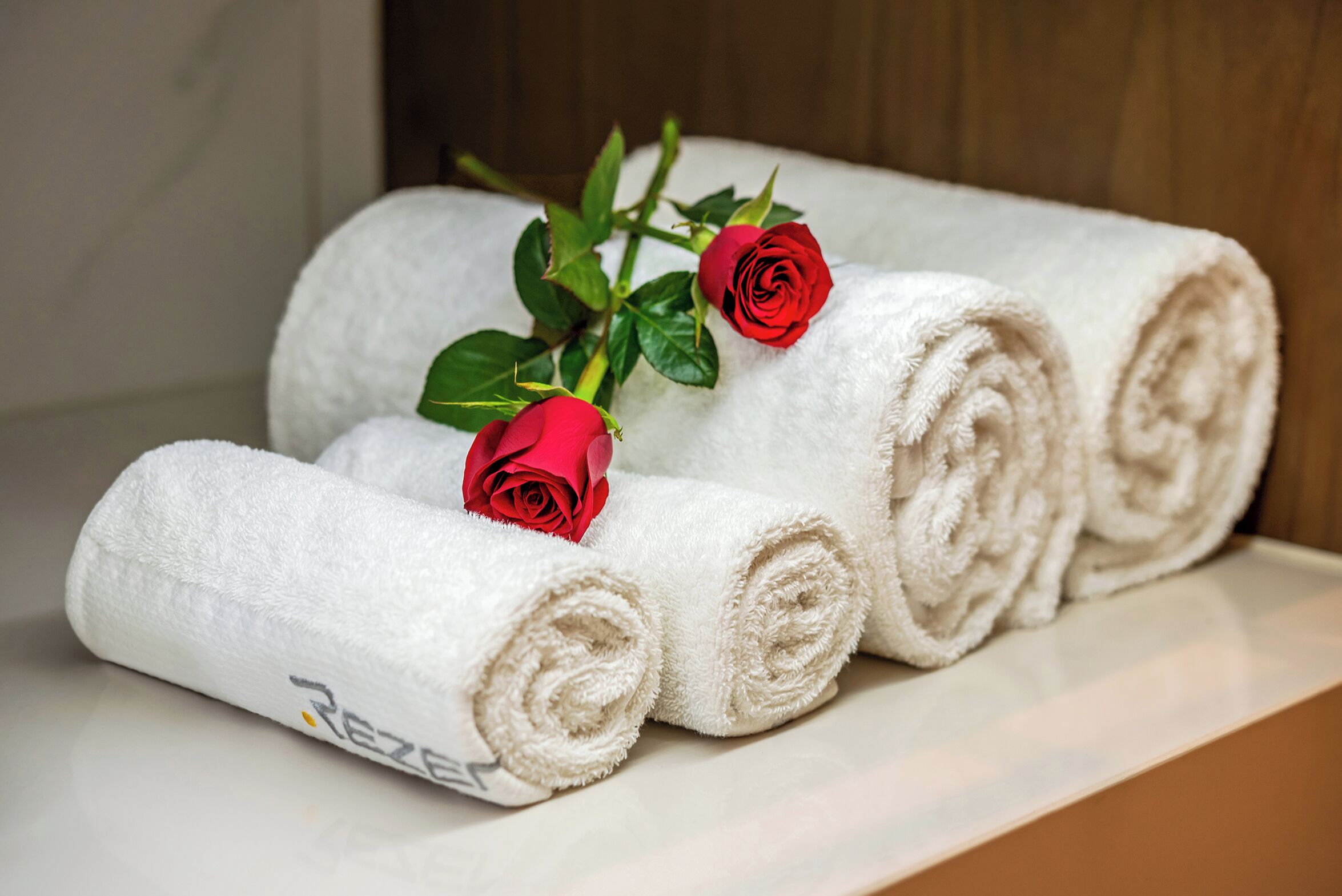 Three rolled towels and two red roses on a white surface.