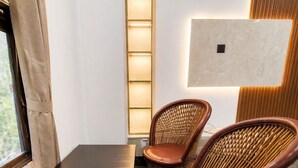 Ein Zimmer mit einem dunklen Holztisch, zwei Korbstühlen mit Ledersitzen, einer Wandleuchte und einer schlichten Wand.