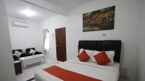A hotel room with a bed, a small table, a chair, a painting on the wall, and an air conditioning unit. - Yasminstar Hotel (Muntok)
